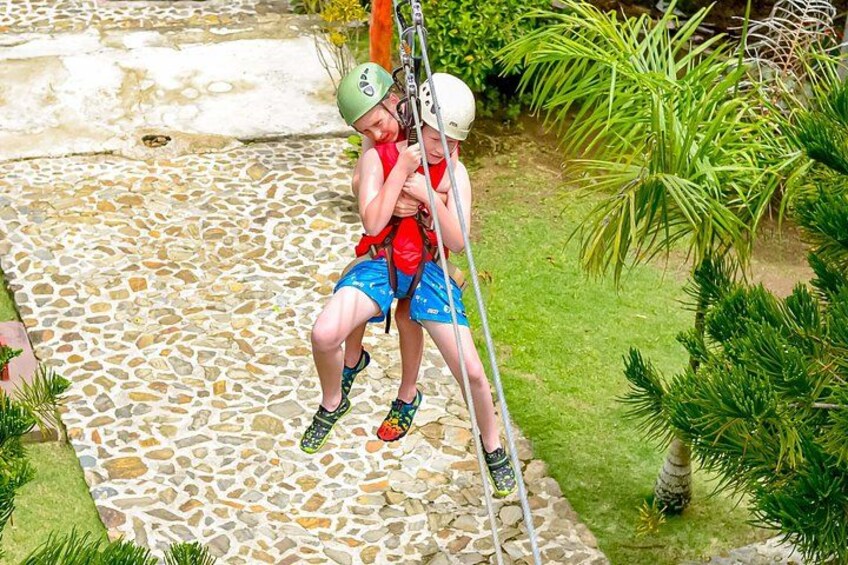 A child climbing a rope ladder in a garden with a stone pathway and green plants. 3
