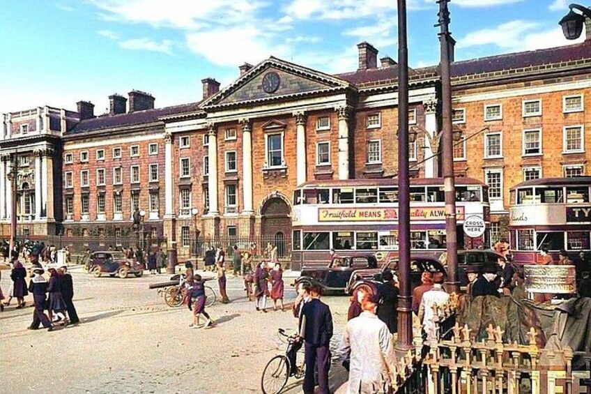 A busy street with vintage cars, pedestrians, and a large building with a clock. 1