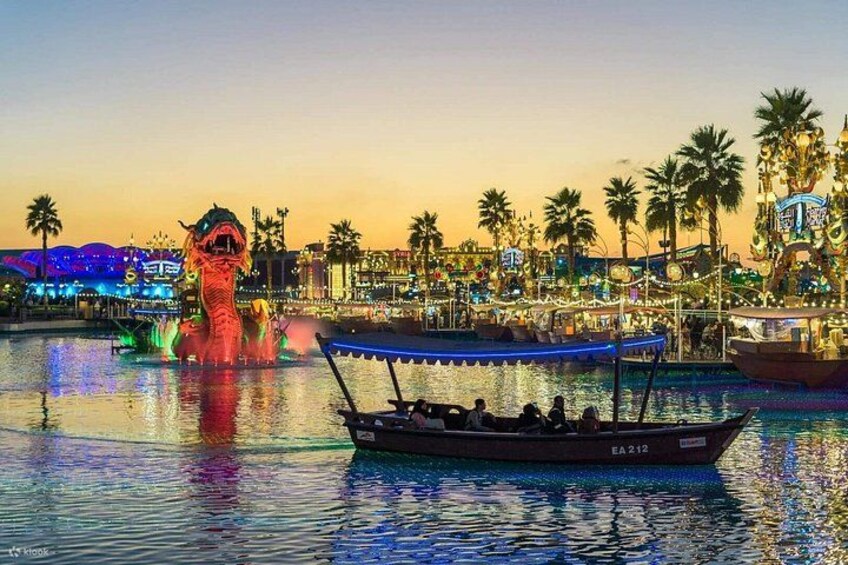 A boat on a body of water with a dragon statue and a brightly lit amusement park in the background. 5