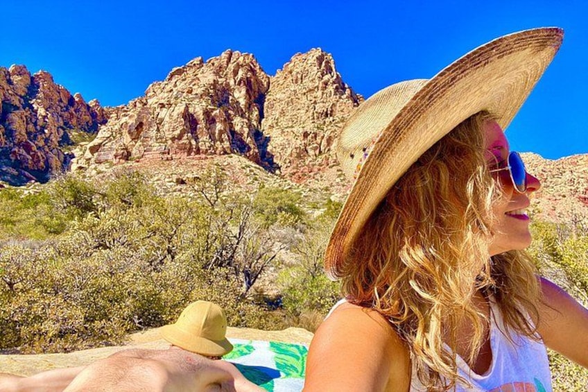 Una persona con sombrero de paja y gafas de sol, paisaje desértico con formaciones rocosas, vegetación escasa y cielo azul despejado. 2