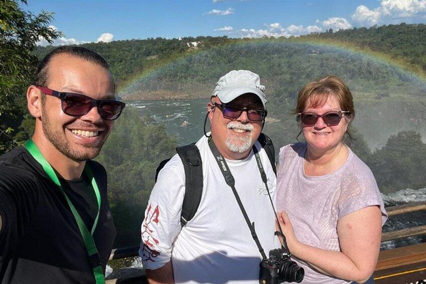 Three people standing by a river with a rainbow in the background. 3