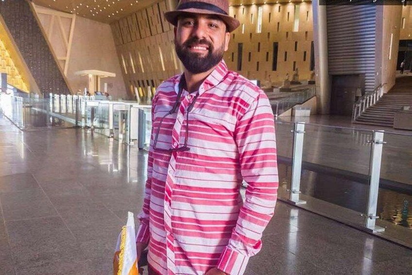 A man in a striped shirt and hat standing in a modern building with glass railings and a staircase. 2