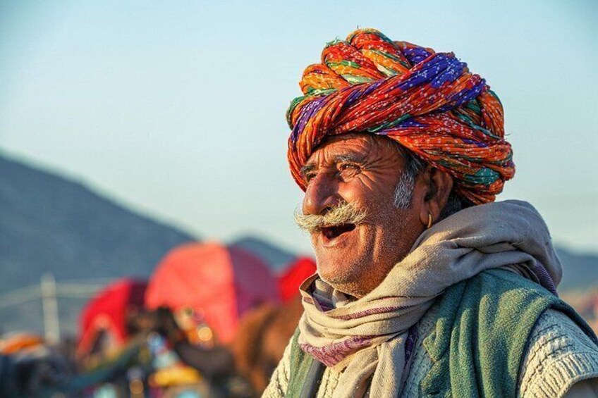 A person wearing a colorful turban and a shawl, with a mountainous background. 2