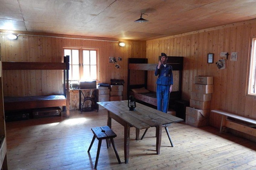 A wooden cabin interior with bunk beds, a table, and a person standing by the window. 3