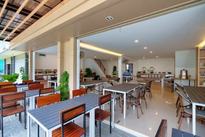 An indoor dining area with wooden tables and chairs, a kitchen in the background, and a staircase leading to an upper level. 5