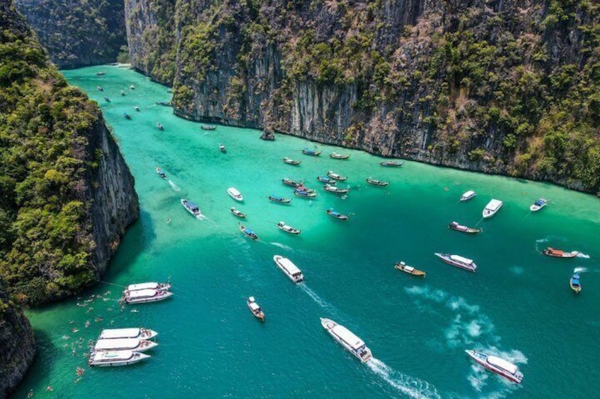 A turquoise river surrounded by steep cliffs with numerous boats anchored along the banks. 1