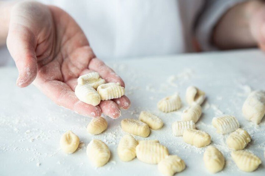 A hand holding and dropping small, round, pale-colored pasta shapes onto a flour-dusted surface. 5