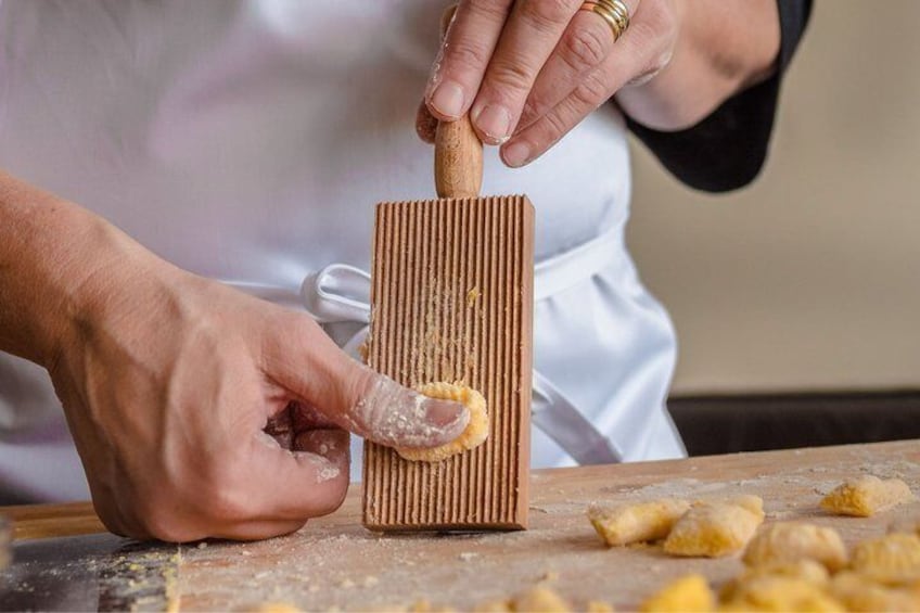 A person using a wooden tool to flatten dough on a surface. 1