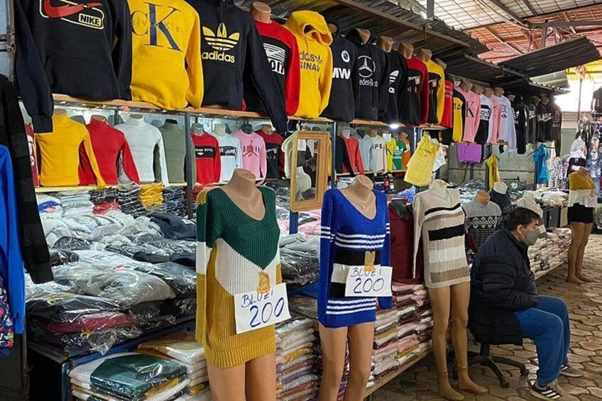 Ein Kleidungsstand mit Schaufensterfiguren, die verschiedene Kleidungsstücke zeigen, darunter T-Shirts und Kleider, mit Preisschildern. 2
