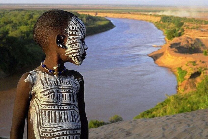 A person with traditional body paint, a river, and a riverbank with vegetation. 5
