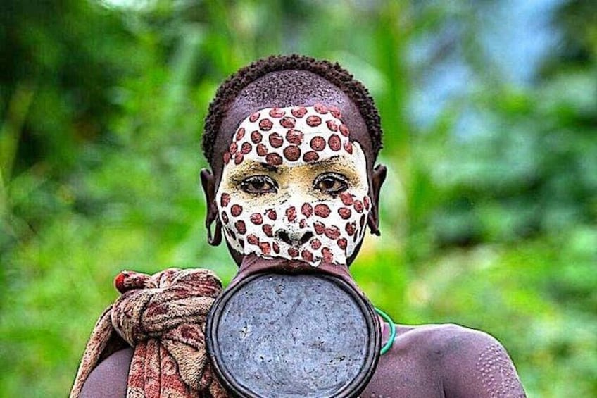 A person with leopard print face paint holding a circular object. 1