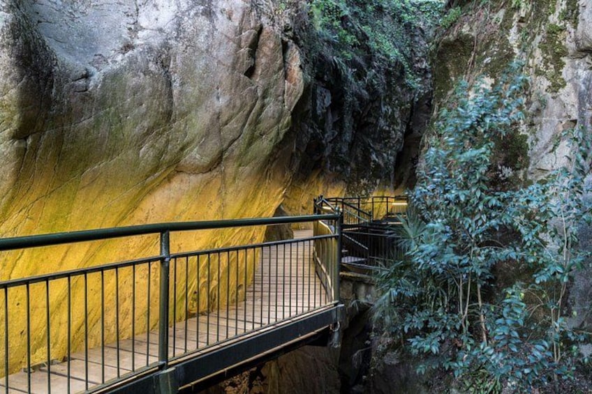 A stone bridge with metal railings, surrounded by greenery and rocky terrain. 3