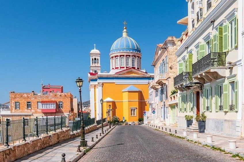 A street leading to a church with a blue dome, colorful buildings, and a clear blue sky. 1