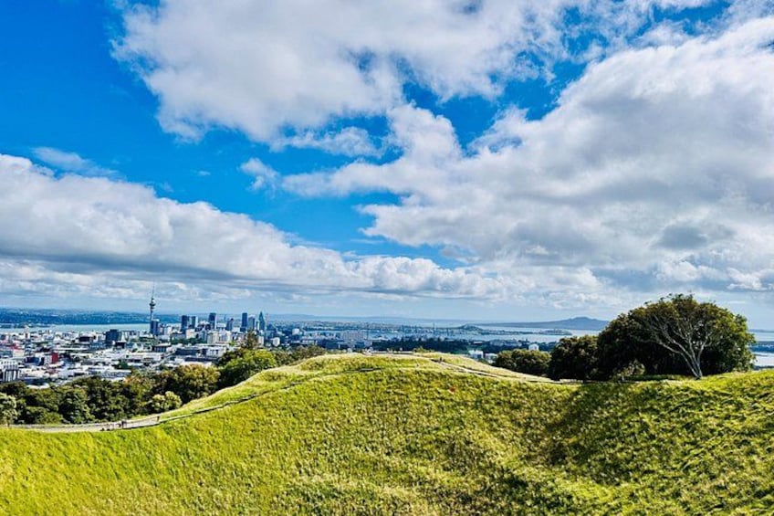 A city skyline with a prominent tower, rolling green hills, and a clear blue sky. 5