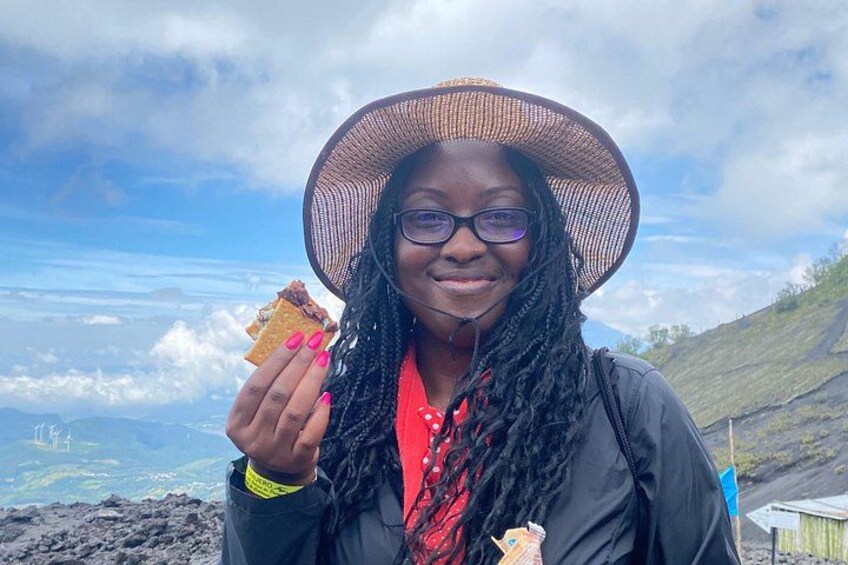 A person holding a chip, wearing a wide-brimmed hat, and standing on a hill with a view of the landscape. 4