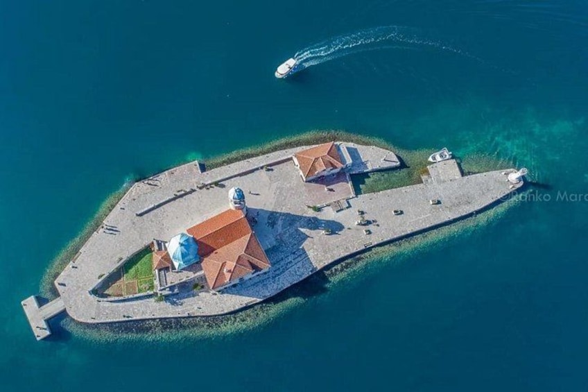 An aerial view of a small island with a large building featuring a red roof, surrounded by clear blue waters. 2
