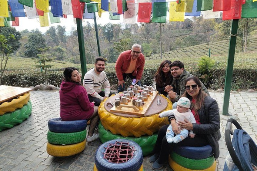 A group of people sitting on colorful tires around a table with drinks, outdoors with a hilly landscape in the background. 2