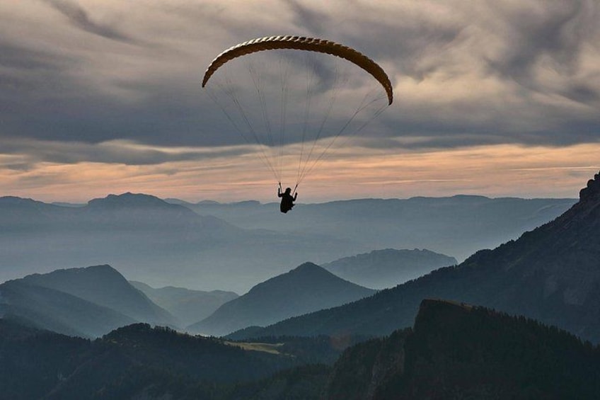 A person paragliding over a mountainous landscape with a cloudy sky. 4