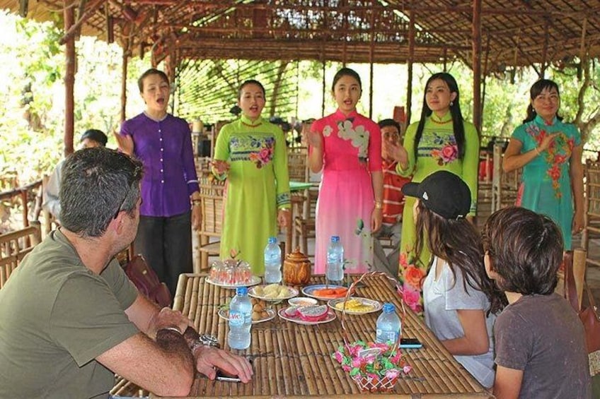 A group of people sitting around a table with food and drinks, under a bamboo structure. 3