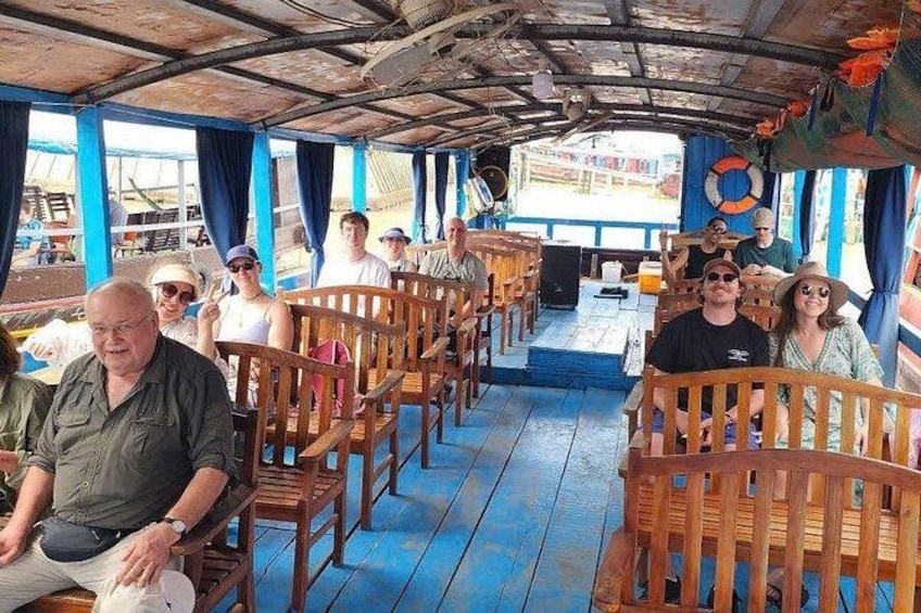 A boat with wooden benches and a blue floor, passengers seated, and a lifebuoy visible. 4