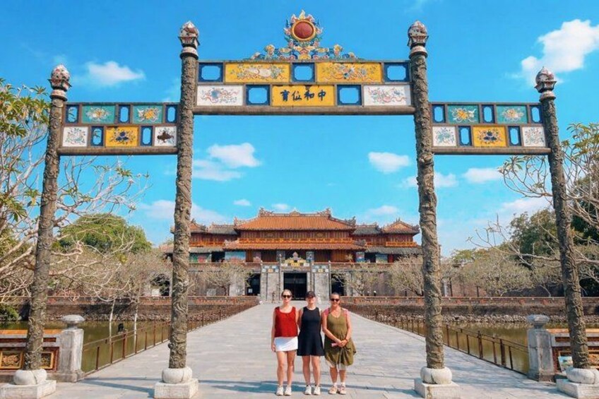 Een traditioneel hek met ingewikkelde versieringen, een heldere lucht en een gebouw met pannendak in de verte. 1