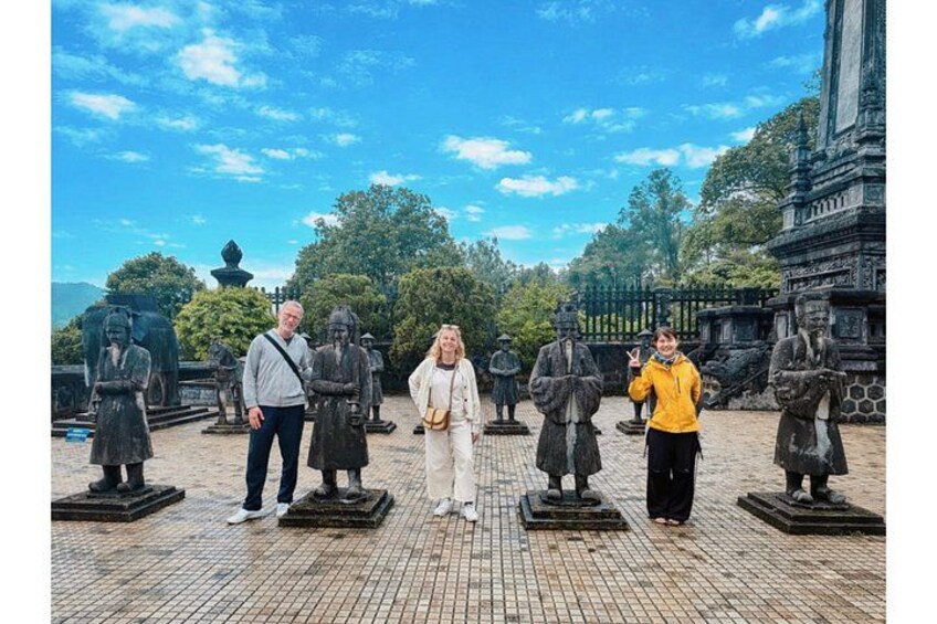 Un groupe de personnes se tient devant des statues, dans un cadre extérieur agrémenté d’arbres et avec un ciel dégagé en arrière-plan. 3