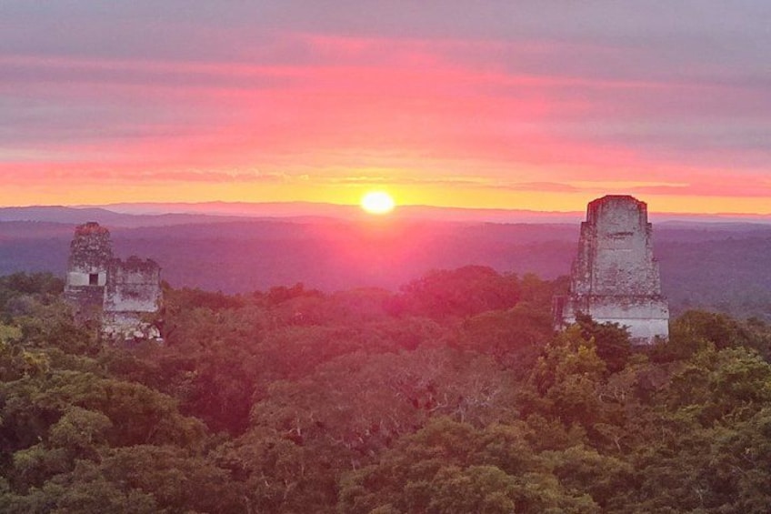 A sunset over a forested landscape with two ancient stone structures. 2