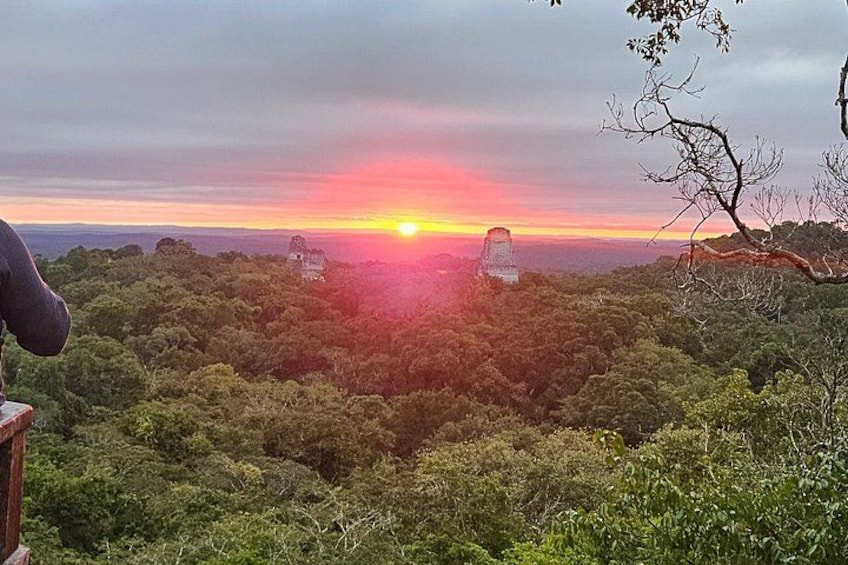 A sunset over a forested landscape with a prominent tower structure. 2