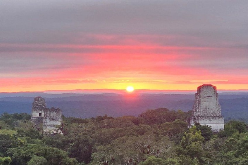 A sunset over ancient ruins surrounded by dense forest. 3