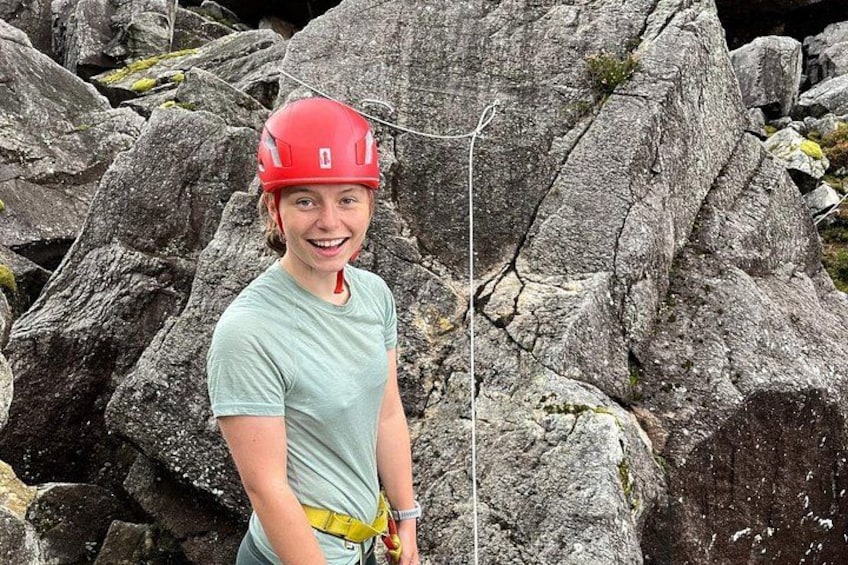 A person wearing a red helmet and a light green shirt standing in front of large rocks. 5