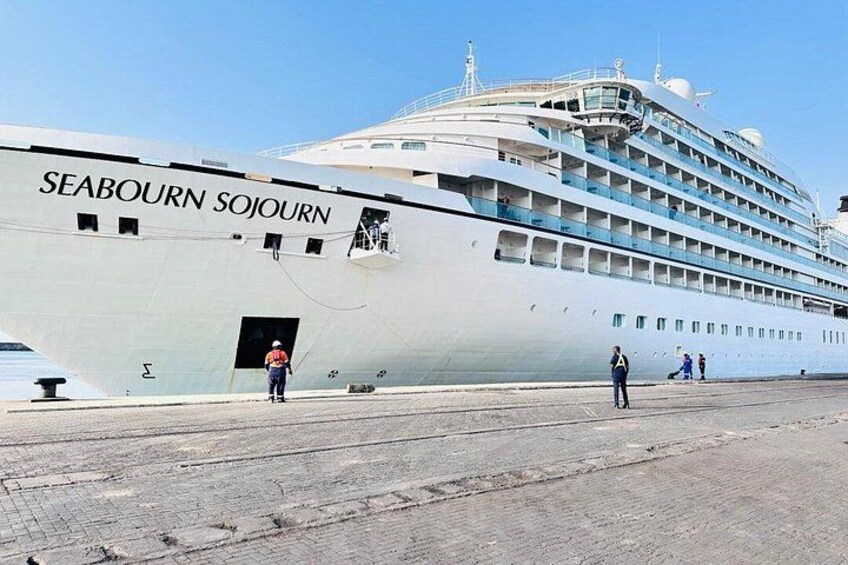 A large cruise ship named SEABOURN SOJOURN docked at a port with people walking around it. 1
