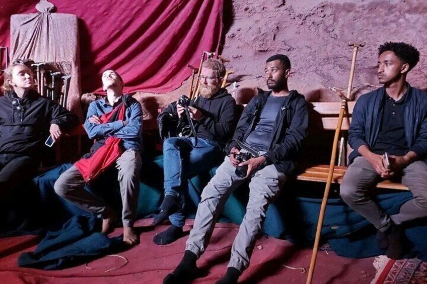 Five people sitting on a couch in a room with a red curtain and wooden furniture. 1
