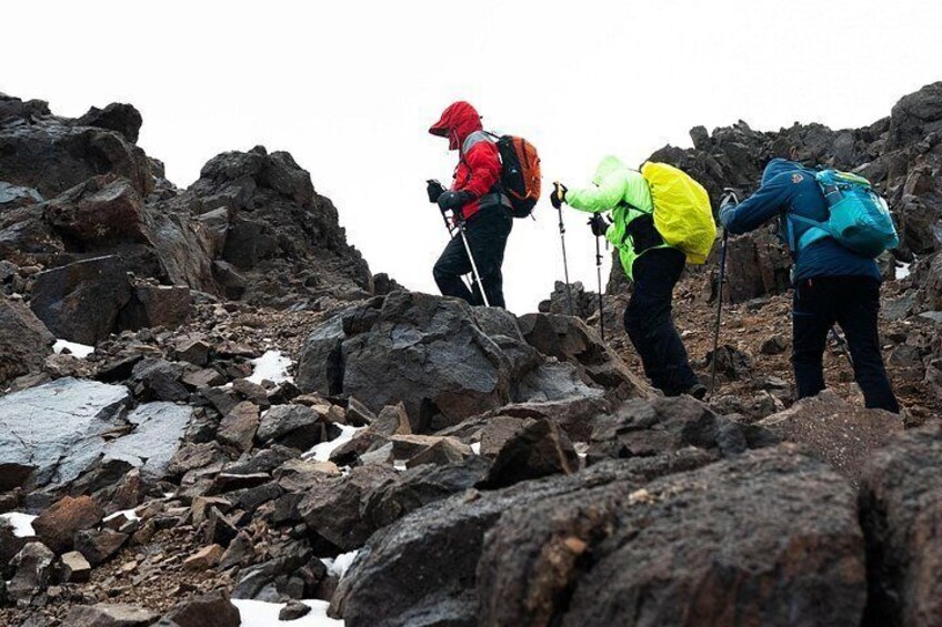 Three hikers on a rocky mountain trail with snow patches. 5