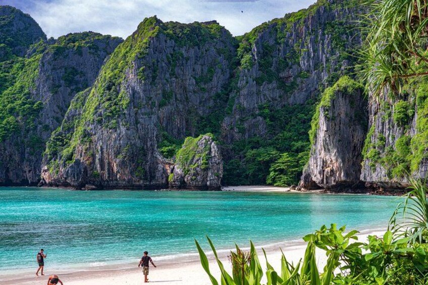 A beach with clear turquoise water, rocky cliffs, and lush greenery. 2