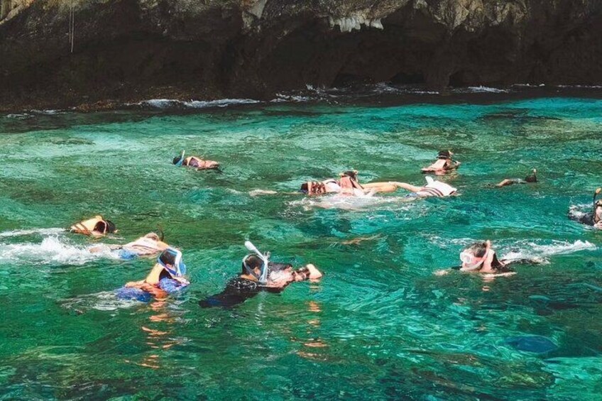 People swimming in a clear blue pool surrounded by rocky cliffs. 3
