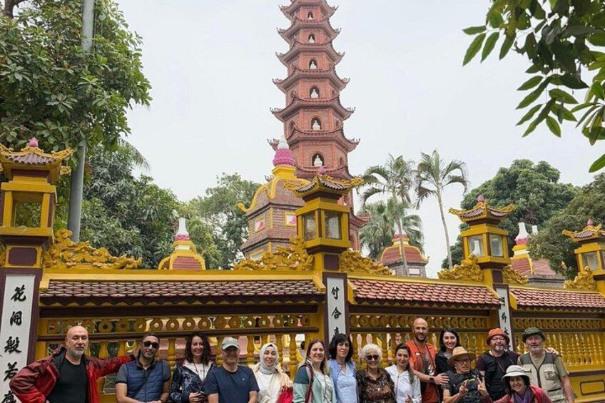 A group of people in front of a temple with a tall pagoda, surrounded by trees. 5