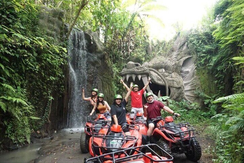 Persone su veicoli ATV vicino a una cascata e a una grande scultura a forma di drago in una foresta. 1