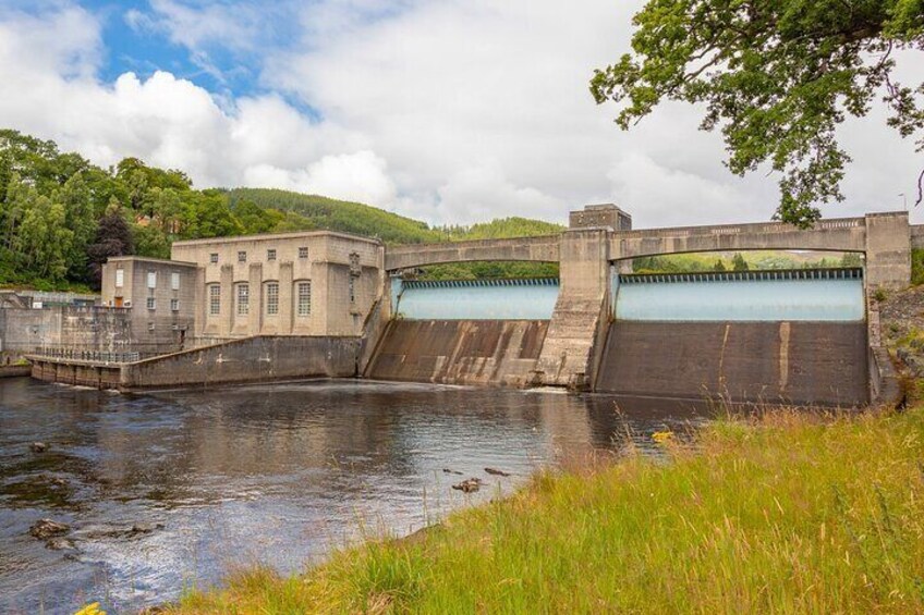 A dam with water flowing through it, surrounded by greenery and a clear sky. 4