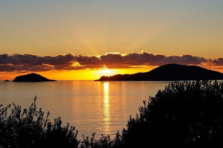 A sunset over a calm body of water with silhouettes of landforms and vegetation in the foreground. 5