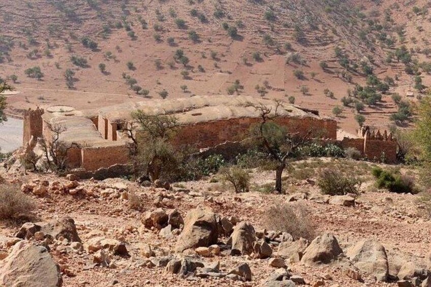 A desert landscape with a ruined structure, sparse vegetation, and a distant hill. 2
