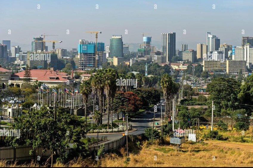 A cityscape with a mix of modern and older buildings, a construction site, and a park with trees and a pathway. 4