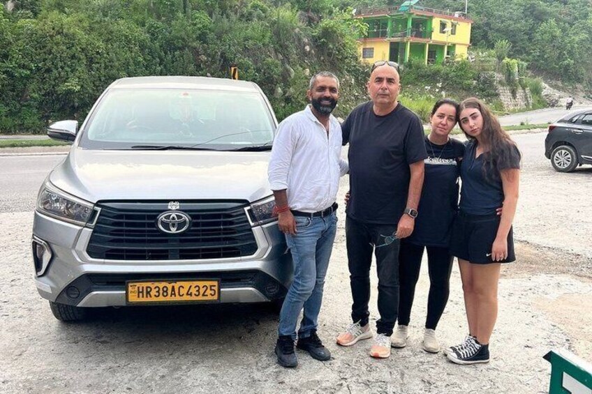 A group of people standing in front of a silver Toyota car with a visible license plate. 5