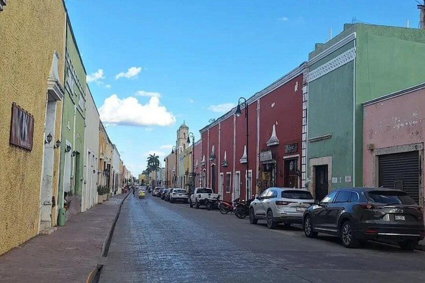 Calle flanqueada por edificios coloridos, coches aparcados y un cielo despejado. 4
