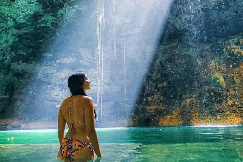 Eine Person in einem Bikini steht in klarem Wasser, im Hintergrund ein Wasserfall. 2