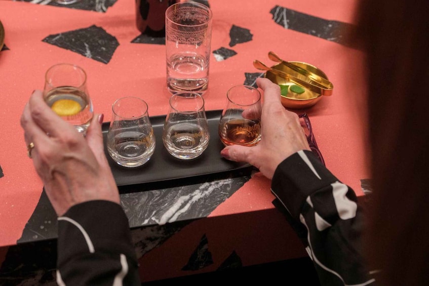 A person holding a tray with several glasses of a beverage, a glass of water, and a small bowl with a green object. 5