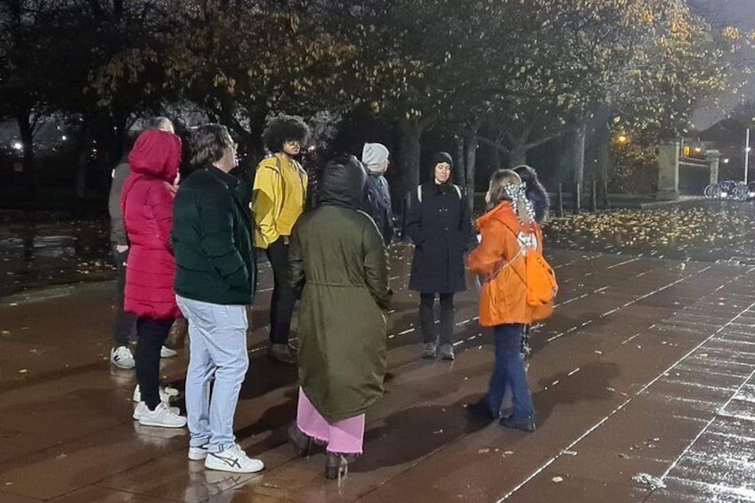 Un grupo de personas de pie sobre un pavimento mojado por la noche. 5
