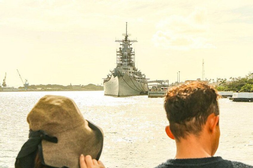 Un gran buque de guerra atracado en un puerto, con una persona sosteniendo un sombrero en primer plano. 2