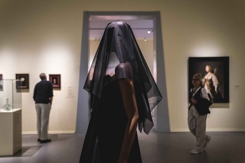 A person in a dark, semi-transparent garment in an art gallery. 3