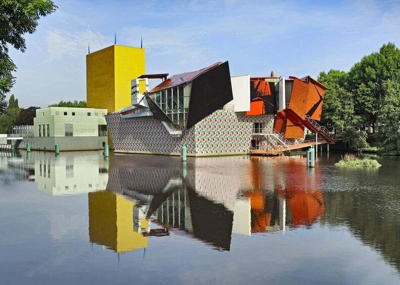 A modern architectural structure with a yellow tower, a large black slanted roof, and a patterned facade, reflecting on the water. 1
