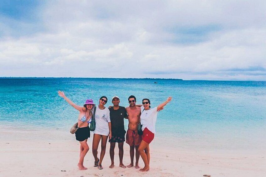 A group of people on a beach with clear blue water and a cloudy sky. 2
